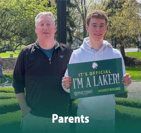 A dad posing with his son who has decided to attend Ѹ. The son holds a poster reading "It's Official. I'm a Laker!"